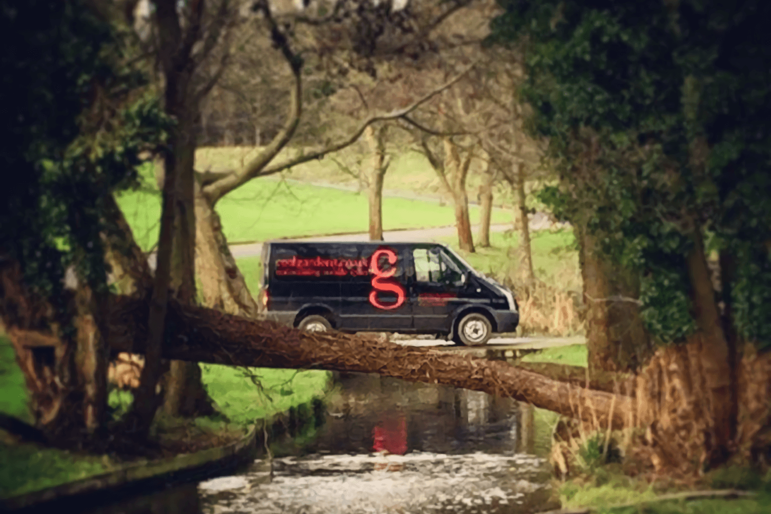 A black and red cool gardens van parked next to a river with trees