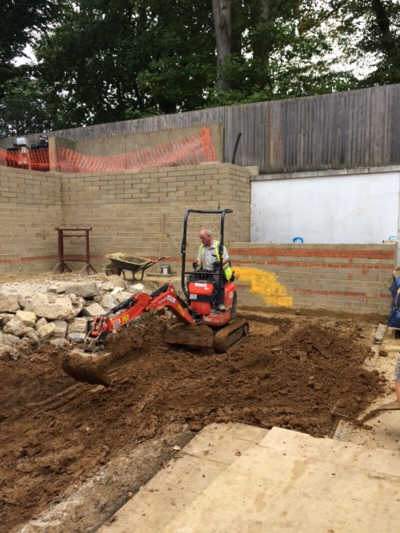 A garden space under construction with a man using a digger