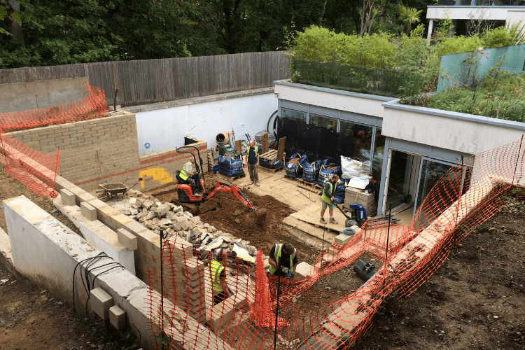 a view of a garden under construction with workers digging and a pile of rubble