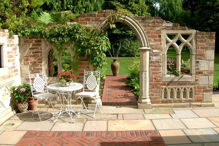 A patio area with a table and chairs in front of a folly leading to the garden