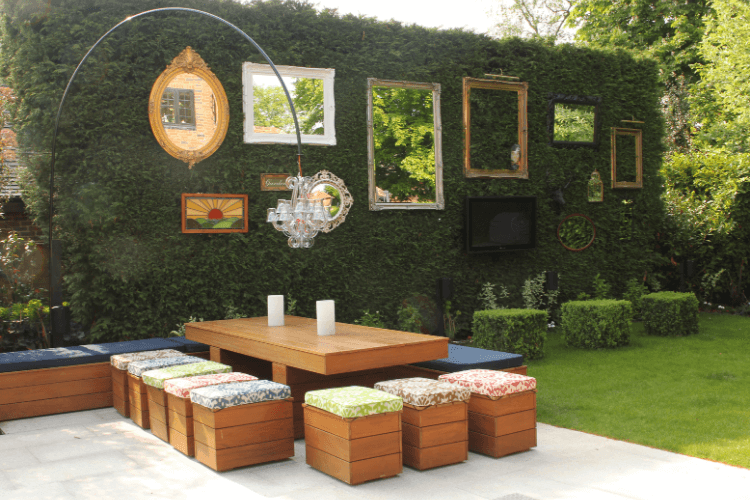 A modern outdoor seating area with mirrors hanging on a hedge