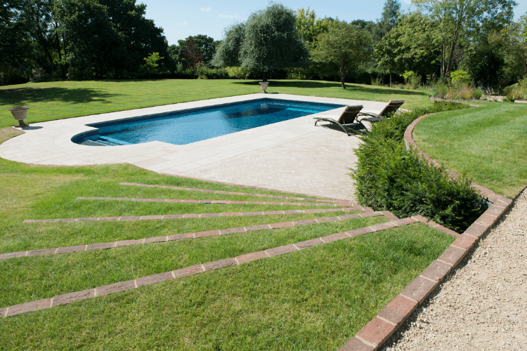 Rectangular outdoor swimming pool positioned within an open lawned garden, with generous paving and minimal planting